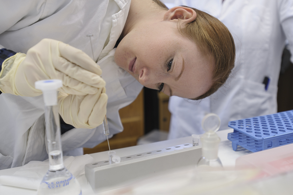 junge Frau mit weißer Schutzkleidung beugt sich über Pipette